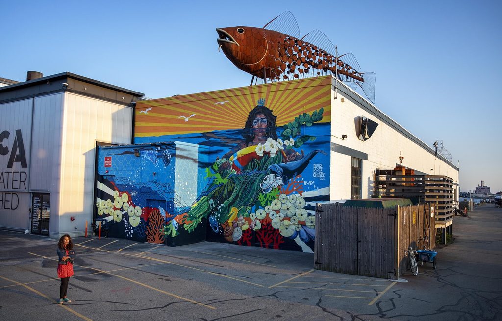 Artist Silvia López Chavez by her mural "Rise" at the Boston Harbor Shipyard and Marina in East Boston. (Robin Lubbock/WBUR